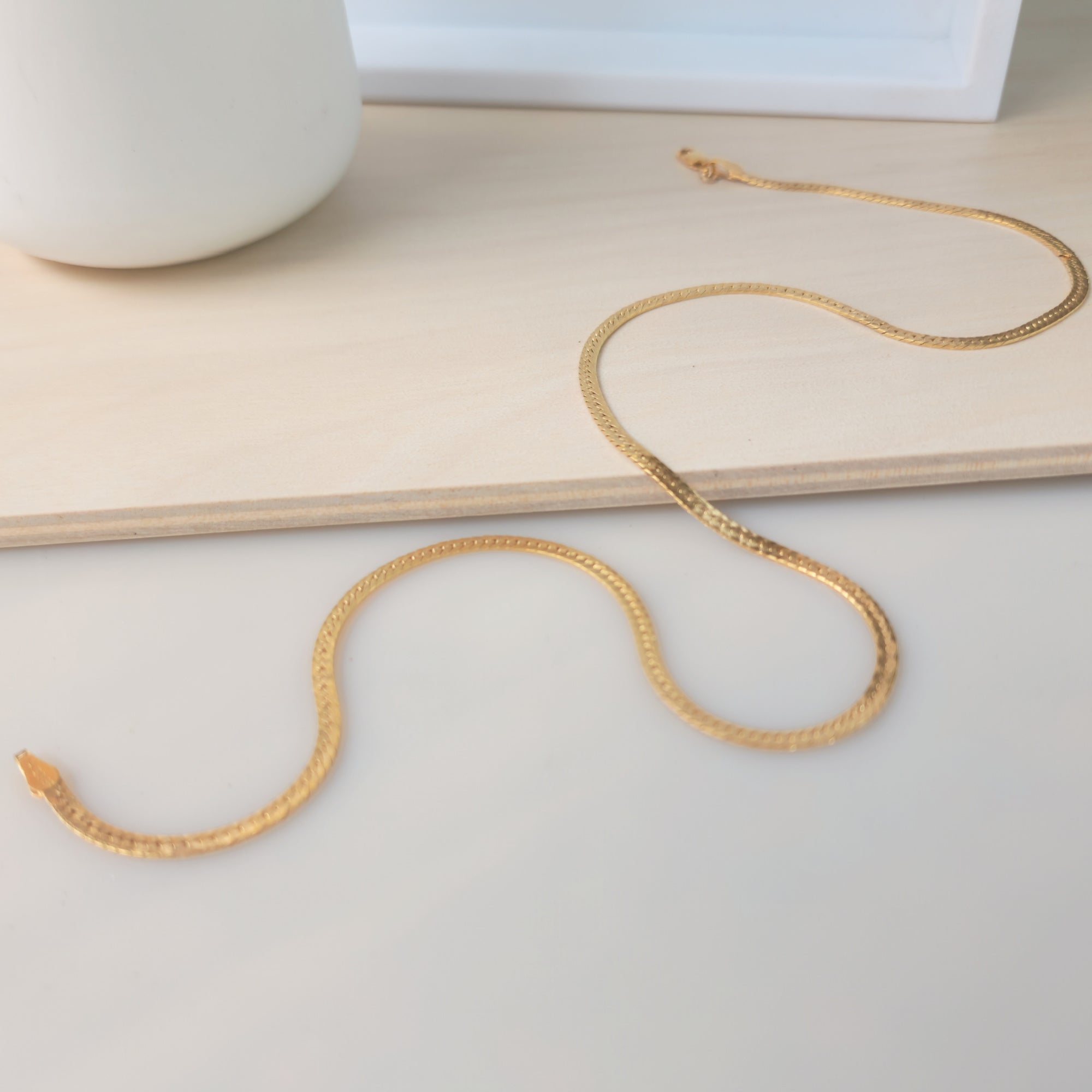 A gold herringbone necklace with a lobster clasp, laid out on a flat surface.