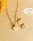 Three 14K solid gold dainty initial necklaces with round engraved tags on wood background