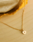 Flat lay of 14K solid gold dainty initial necklace on soft beige fabric