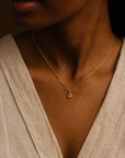 14K solid gold dainty initial necklace worn by woman with dark skin and linen blouse, handcrafted jewelry close-up