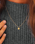 Woman wearing 14K solid gold dainty initial necklace over a gray sweater