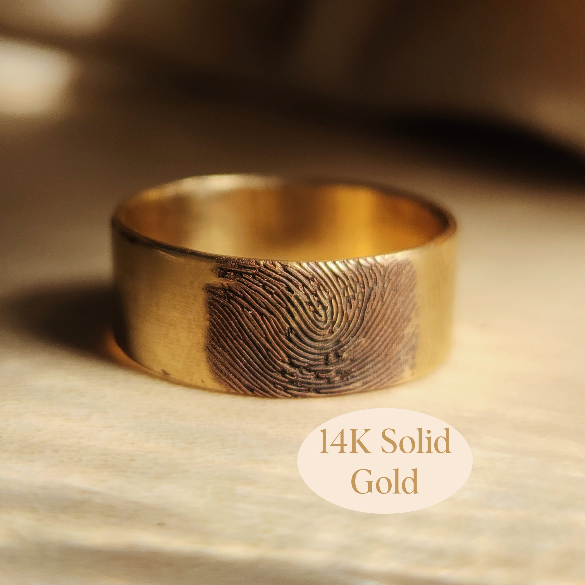 Close-up of 14K solid gold fingerprint band on wood background with gold engraving detail