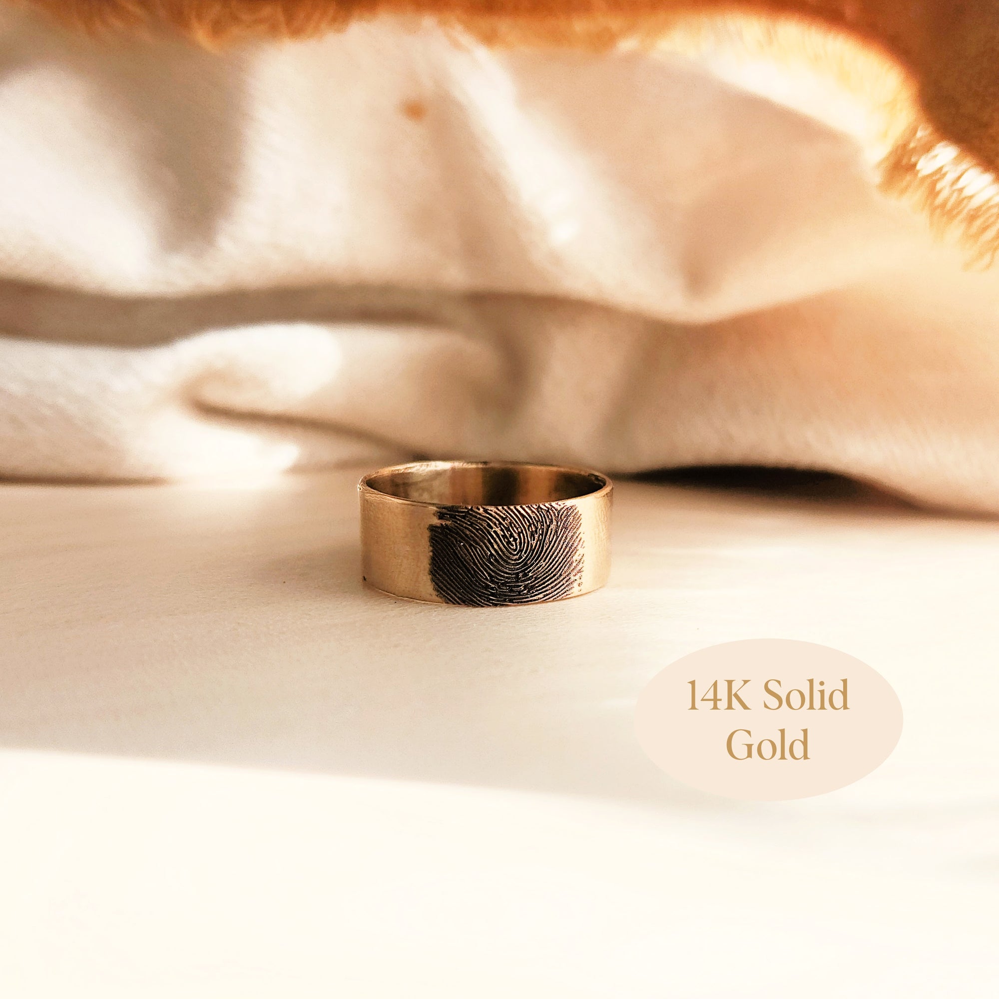 Flat lay of 14K solid gold fingerprint band resting on ivory satin cloth