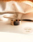 Flat lay of 14K solid gold fingerprint band resting on ivory satin cloth