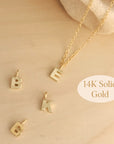 Flat lay of 14K solid gold initial pendant necklace with B, K, and E charms on wood background