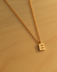 Close-up of 14K solid gold initial pendant necklace with E charm on wood surface