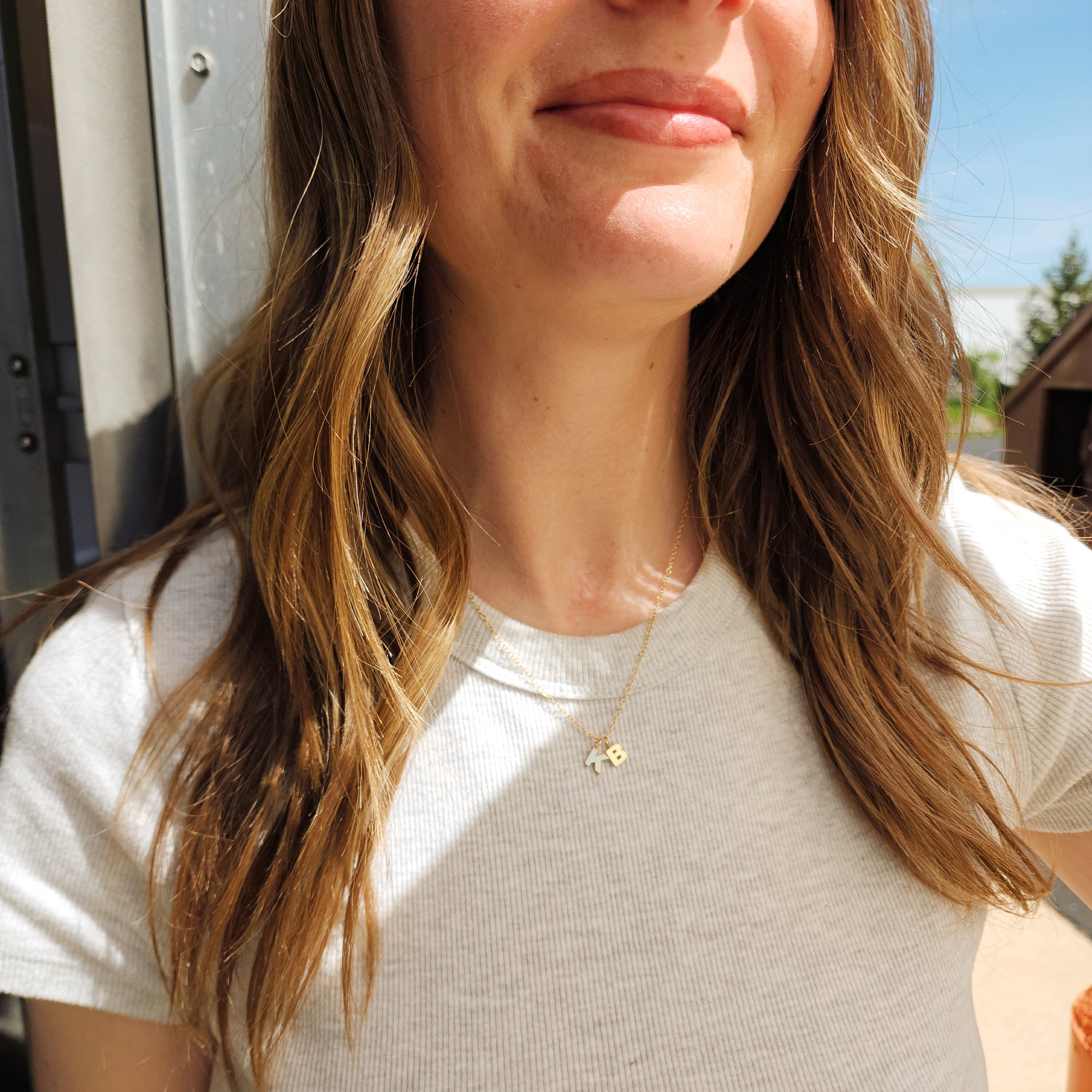 Woman wearing 14K solid gold initial pendant necklace with white shirt and loose waves