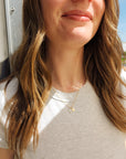 Woman wearing 14K solid gold initial pendant necklace with white shirt and loose waves