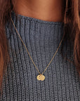 Close-up of two round tags on 14K solid gold name necklace over light wood