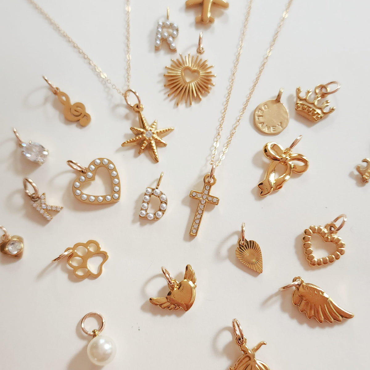 Close-up of 18k gold plated PVD add-on charms on dainty gold chain featuring star, heart, sun, and pearl charms