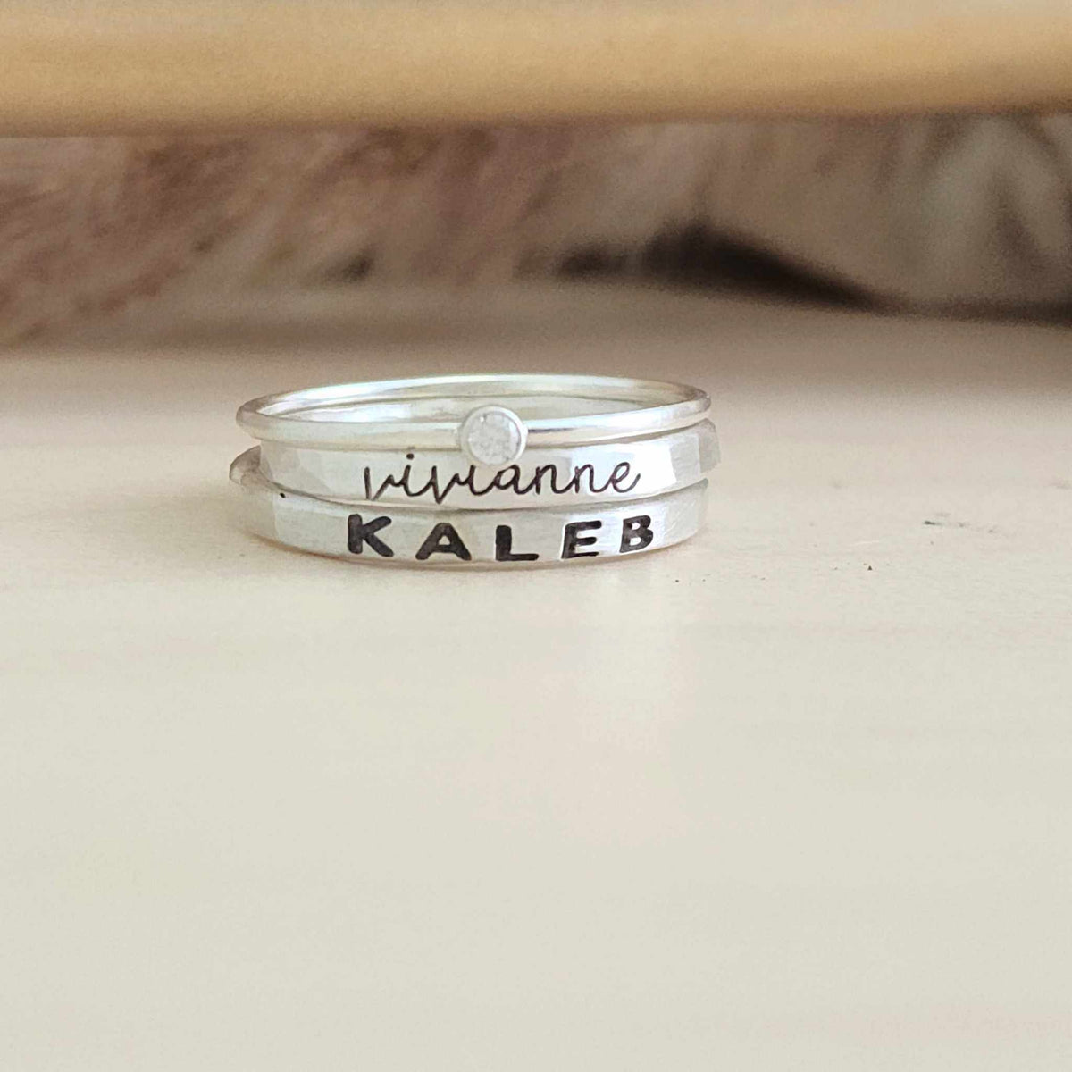 The Maddy Stacking Name Ring Set featuring two personalized name rings and a clear birthstone ring in silver and gold finishes