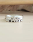 A set of stackable silver rings, with one clear cz ring and two personalized name rings, displayed on a wooden surface.