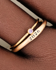 Two rings, one with a plain band and the other featuring a birthstone, displayed on a textured surface with a soft shadow.