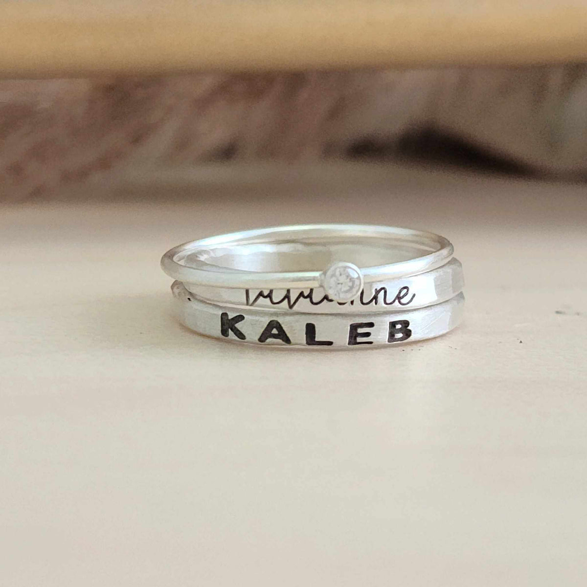 A set of sterling silver rings, including one with a clear cubic zirconia, and two with engraved names in different fonts.