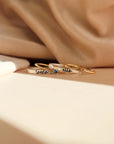 The rings include two thin gold bands with small gemstones and a slightly thicker silver band with engraved names in cursive. One gold ring has a blue gemstone and the engraved name 'laura,' while the other has a clear gemstone. The silver band in the center has the name 'ella' engraved.