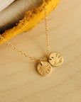 Close-up of 14K solid gold name necklace with two personalized round charms on wood background
