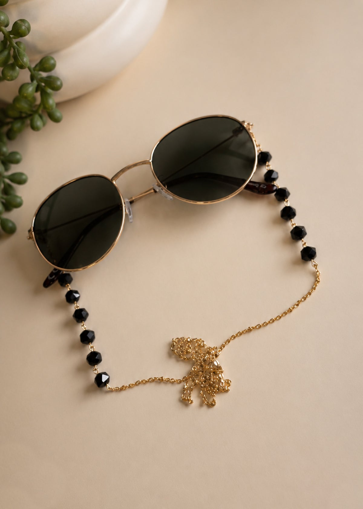 Sunglasses with a decorative chain on a beige surface with a plant in the corner.