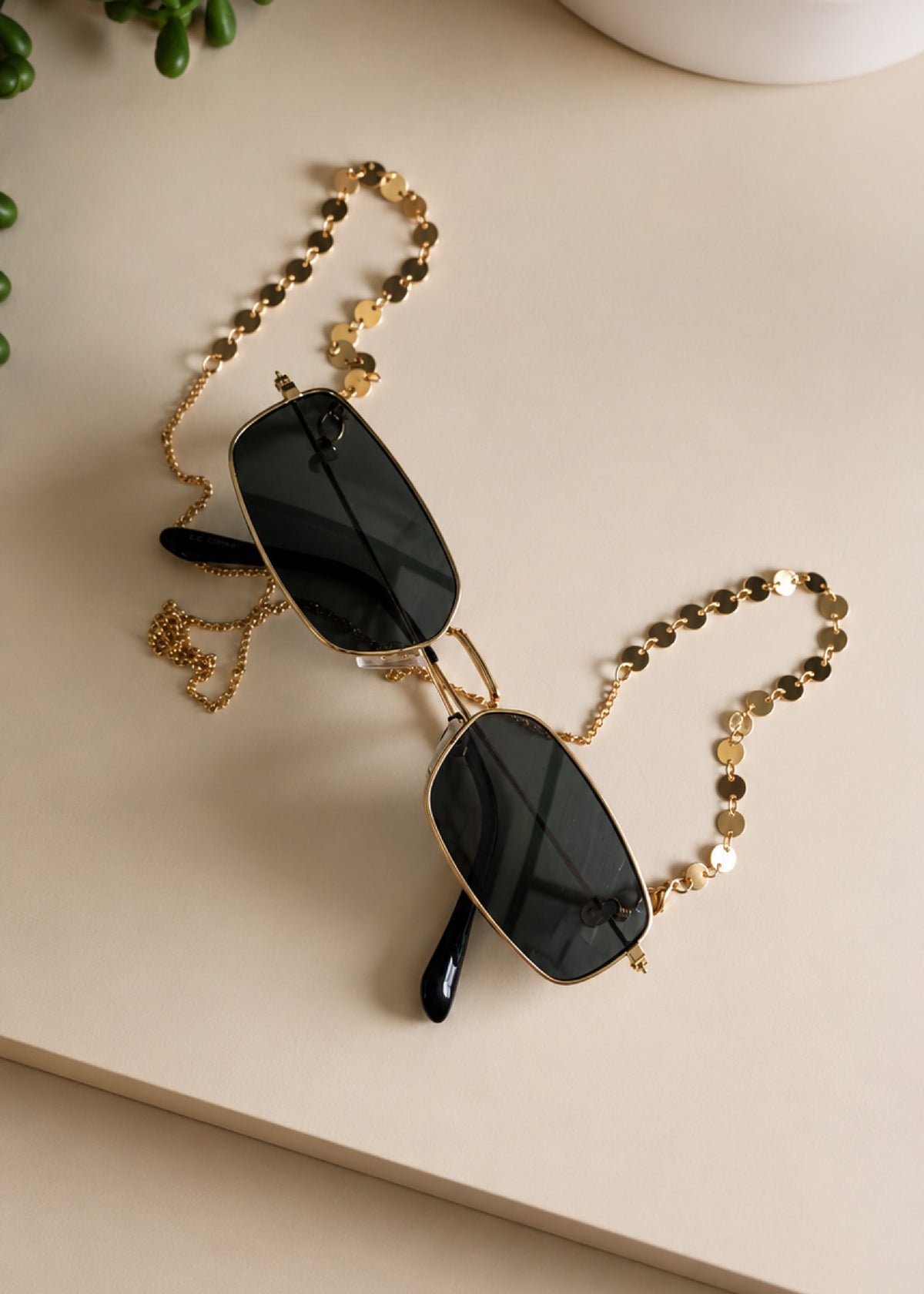 Black sunglasses with a gold chain on a light surface