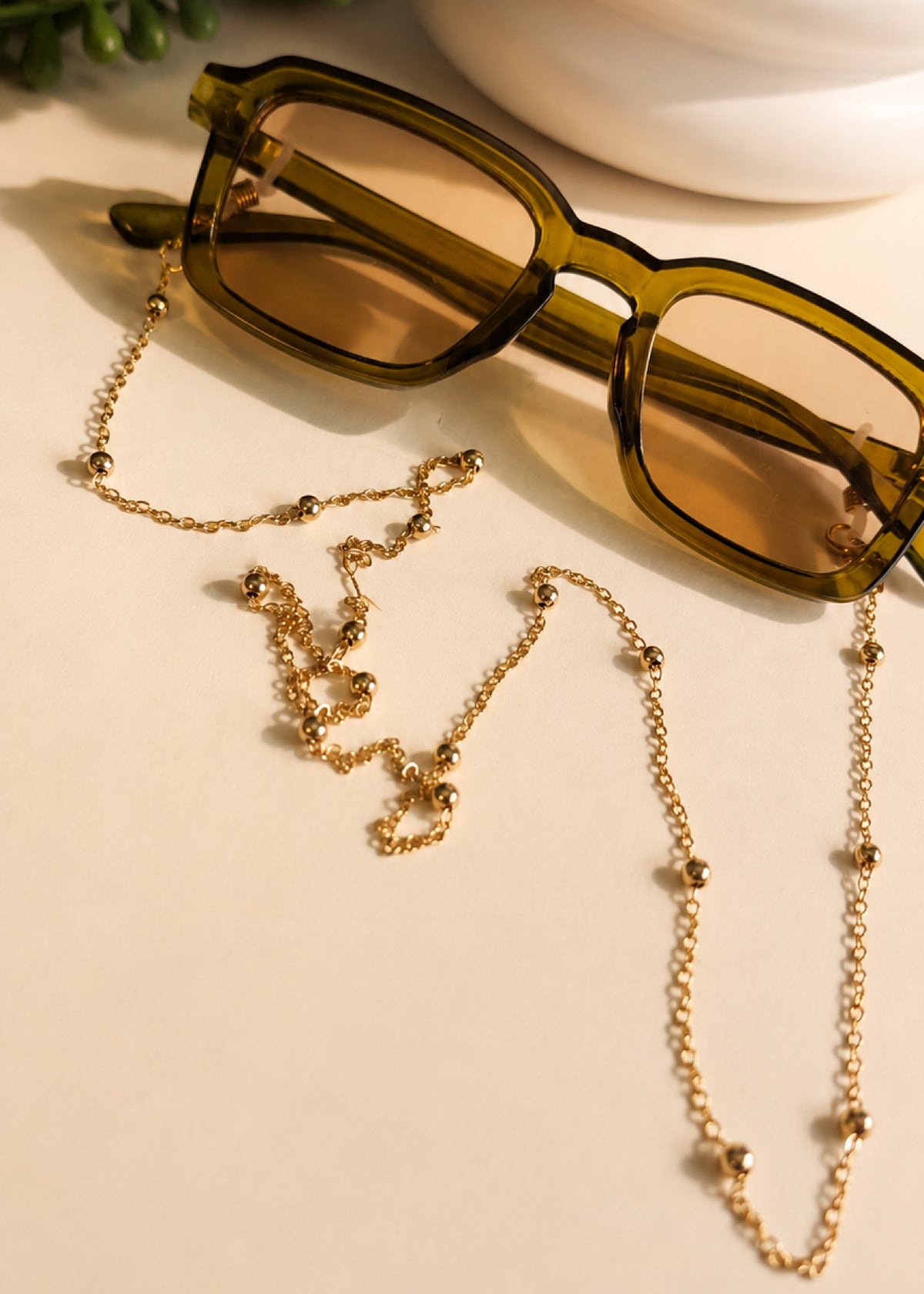 Green sunglasses with a gold chain on a beige surface