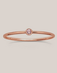 A simple band ring with a single pink gemstone, possibly a birthstone, set in a gold-filled band.