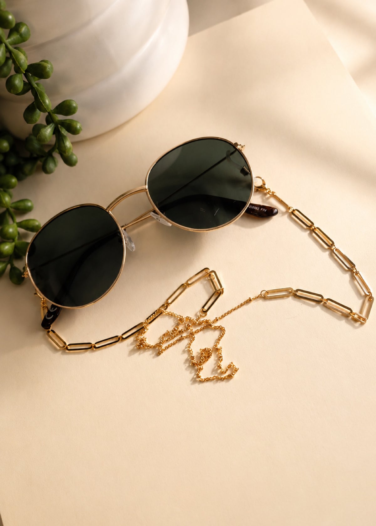 Sunglasses with a gold chain on a light surface with greenery