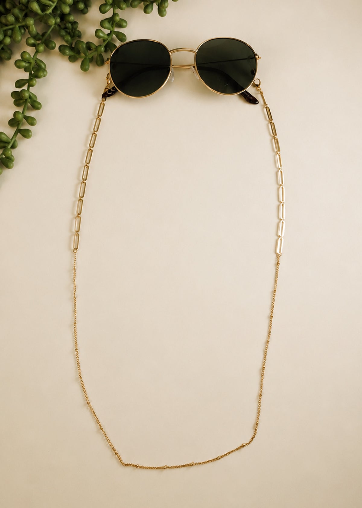 Sunglasses with a gold chain on a beige background