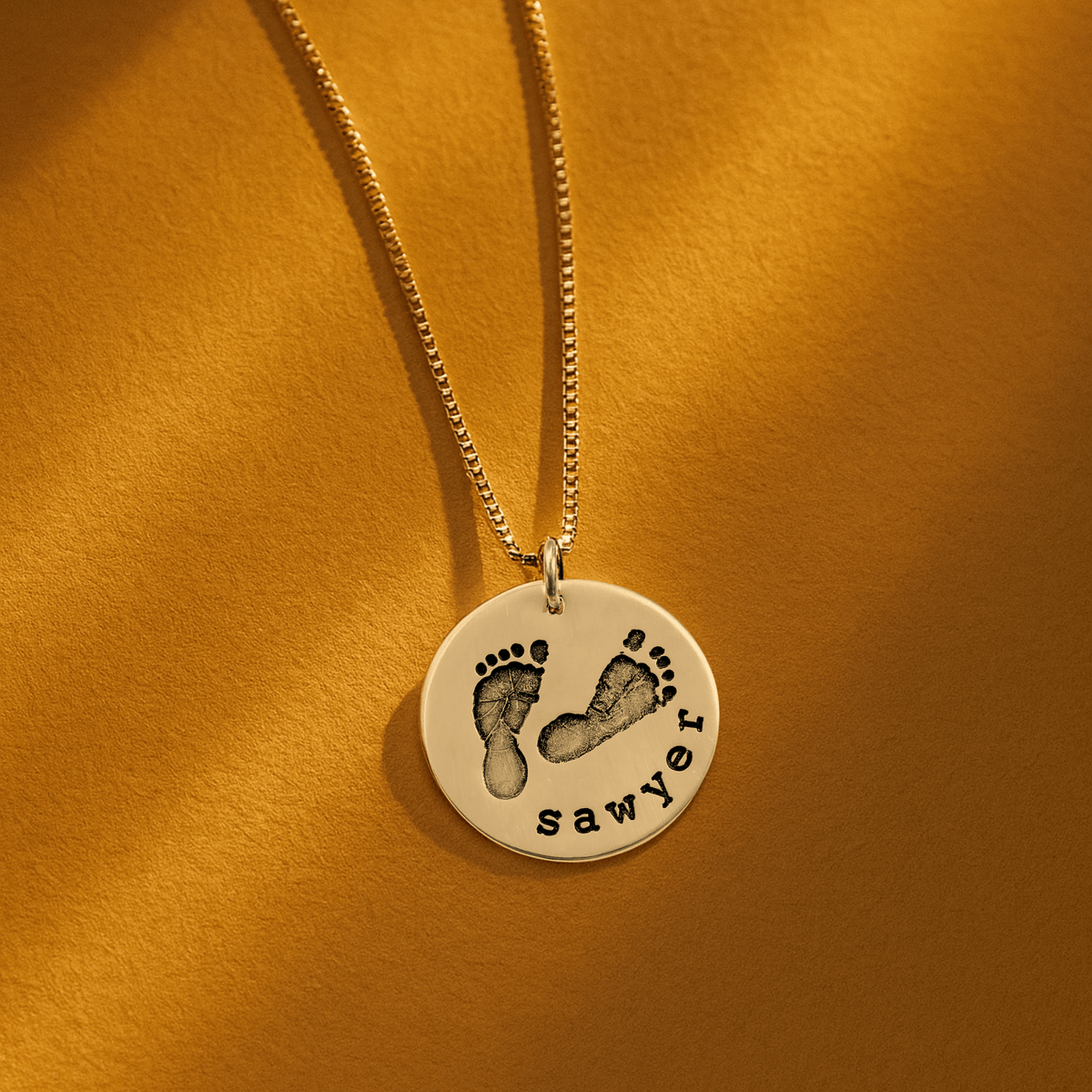 Close-up of a footprint necklace with name engraving on a round pendant in sterling silver