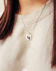 Necklace with a pendant featuring footprints worn by a person in a light-colored sweater.