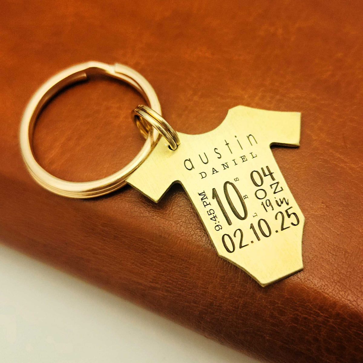 Baby statistics keychain engraved with baby's name, weight, birth time, length, and date on a brushed metal bodysuit keepsake