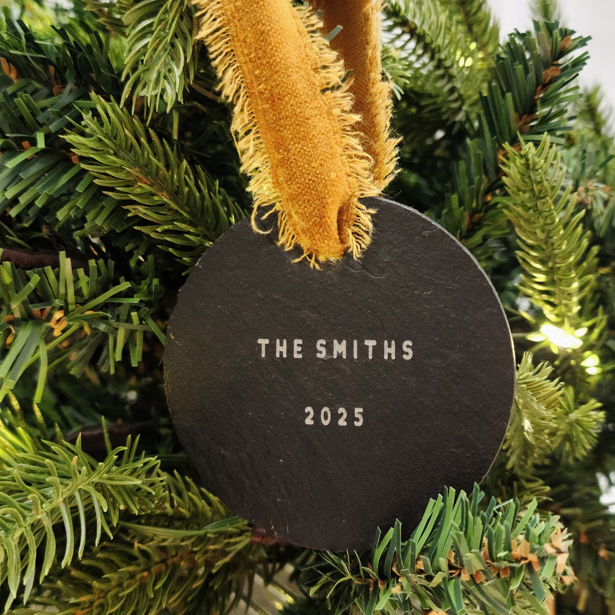 Round black ornament with 'The Smiths' and '2025' text, hanging on a Christmas tree.