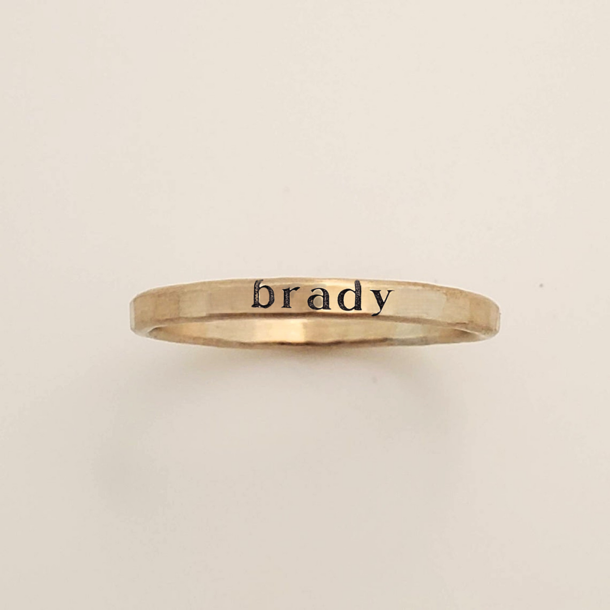 Gold ring with 'brady' engraved on a beige background