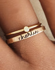 A photo showing a gold-colored ring with the name 'Charlie' engraved on it, worn on a person's finger.