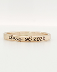 A gold-colored stacking ring with 'class of 2028' engraved on it, displayed against a white background.