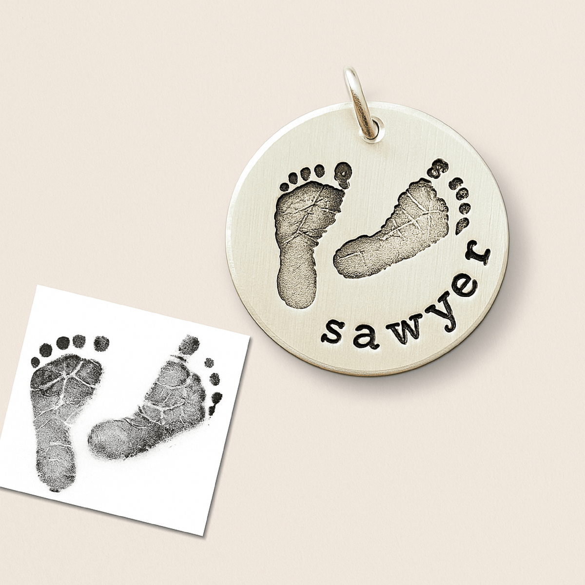 Round silver pendant with footprints and 'sawyer' engraving on a beige background