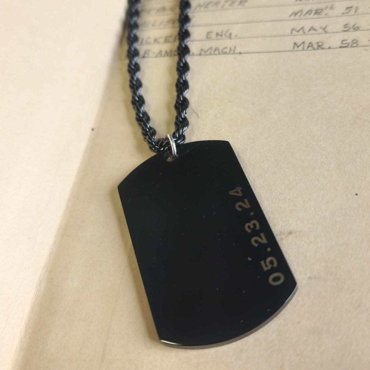 Black dog tag with engraved date on a beige background