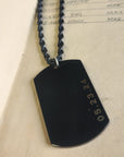 Black dog tag with engraved date on a beige background