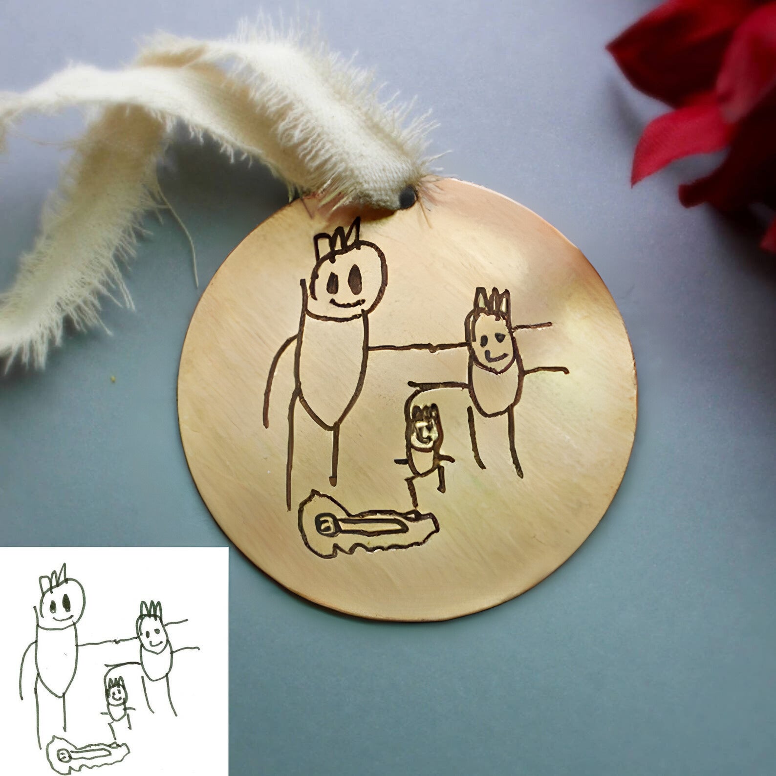 Personalized child art engraved ornament displayed on holiday greenery