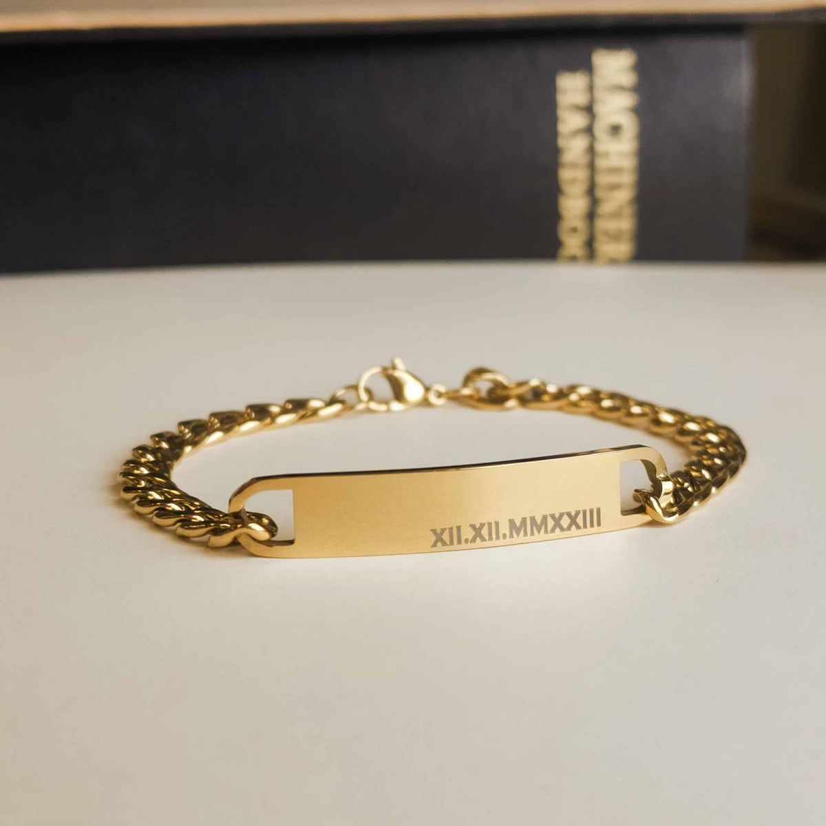 Gold chain bracelet with engraved text on a neutral background