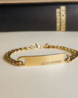 Gold chain bracelet with engraved text on a neutral background