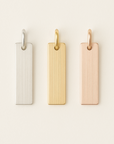 Three rectangular metal tags in silver, gold, and rose gold on a light beige background.