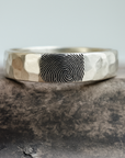 Silver ring with fingerprint engraving on a stone surface