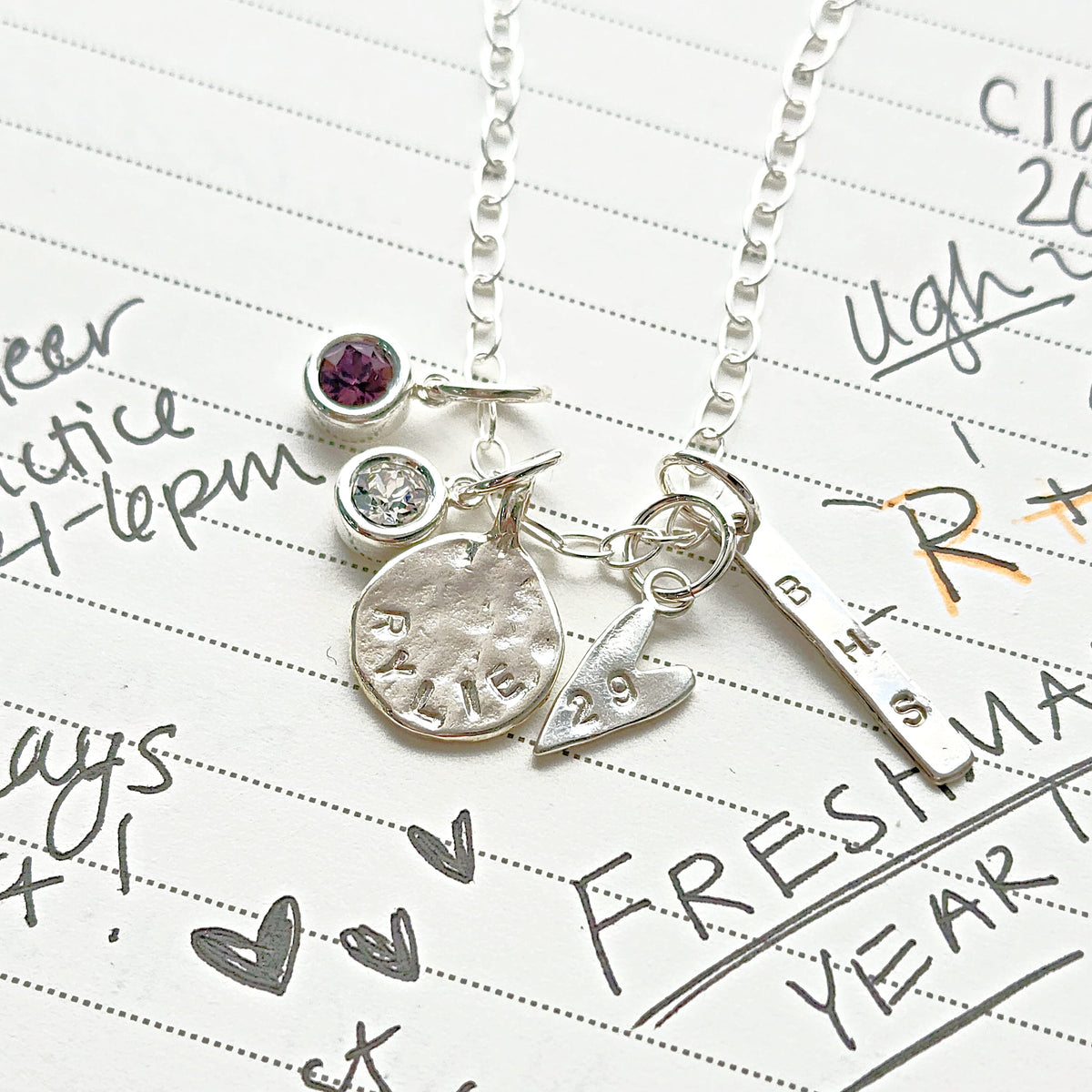 Silver necklace with charms on a piece of paper with writing