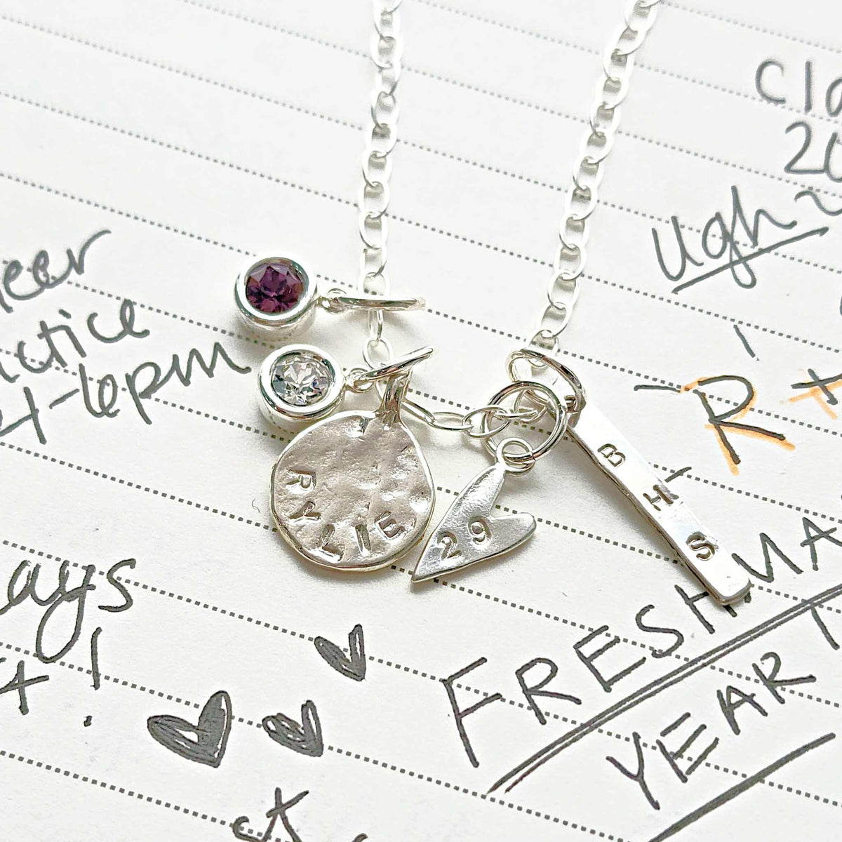Silver necklace with charms on a piece of paper with writing