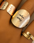 Close-up of custom hammered gold disc ring engraved with names on hand