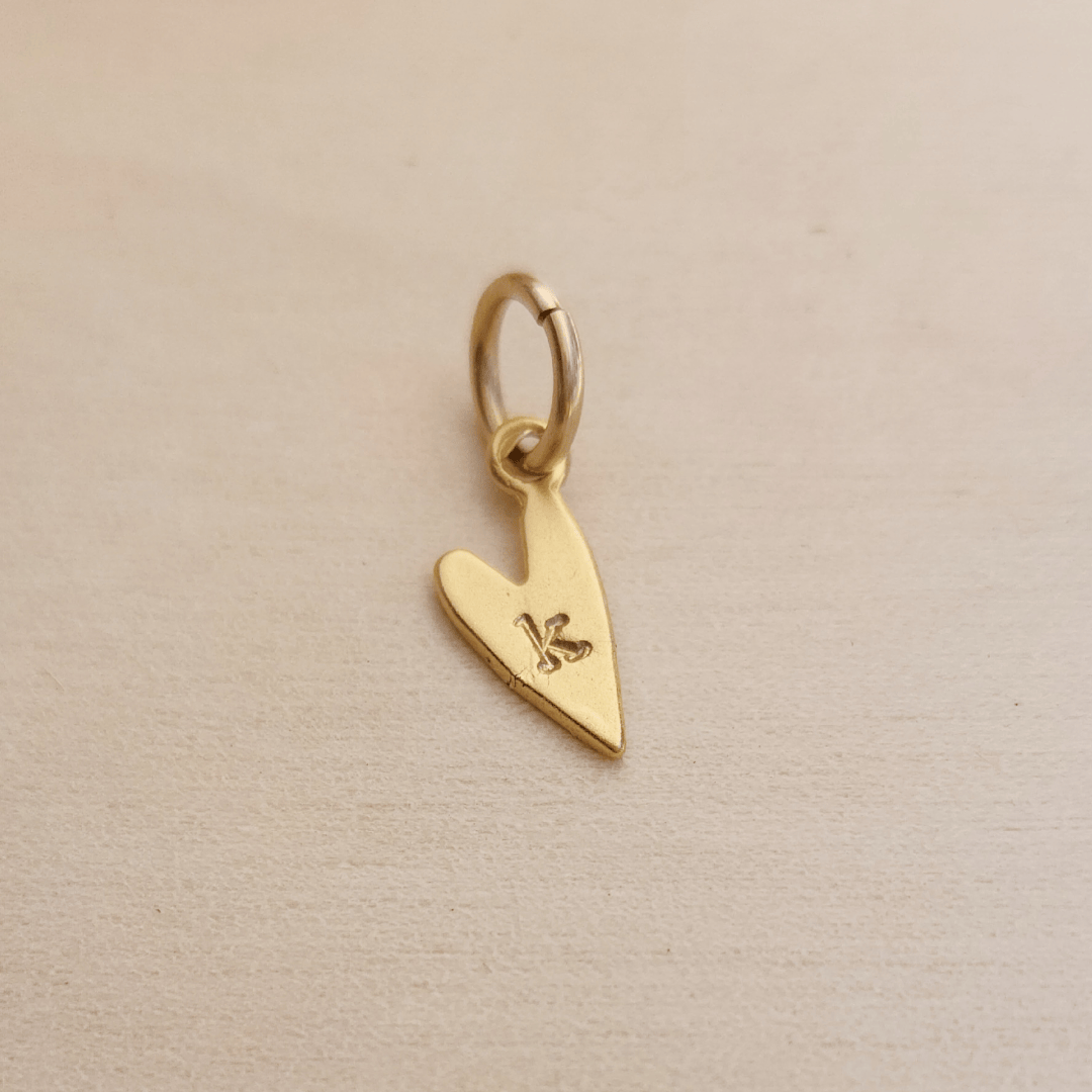 Gold heart-shaped pendant with a letter 'K' on a beige background
