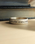 Silver ring with 'MAX JULIAN' engraving on a textured surface with books in the background