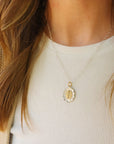 Close-up of a person wearing a gold necklace with a pendant on a plain background