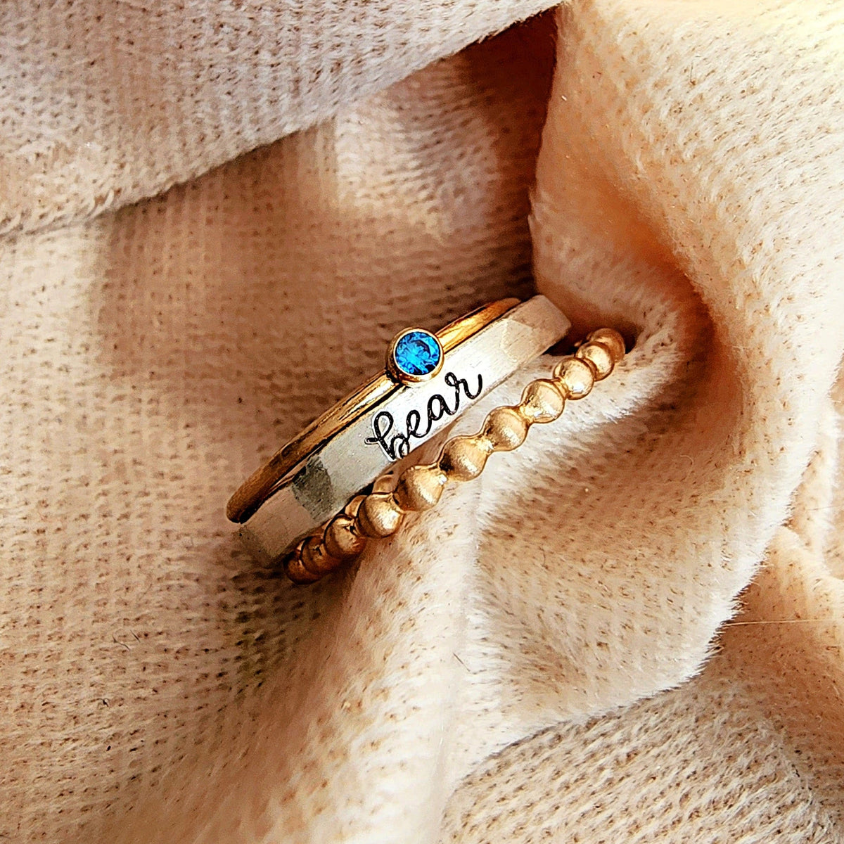 Gold ring with blue gemstone and 'bear' engraving on beige fabric