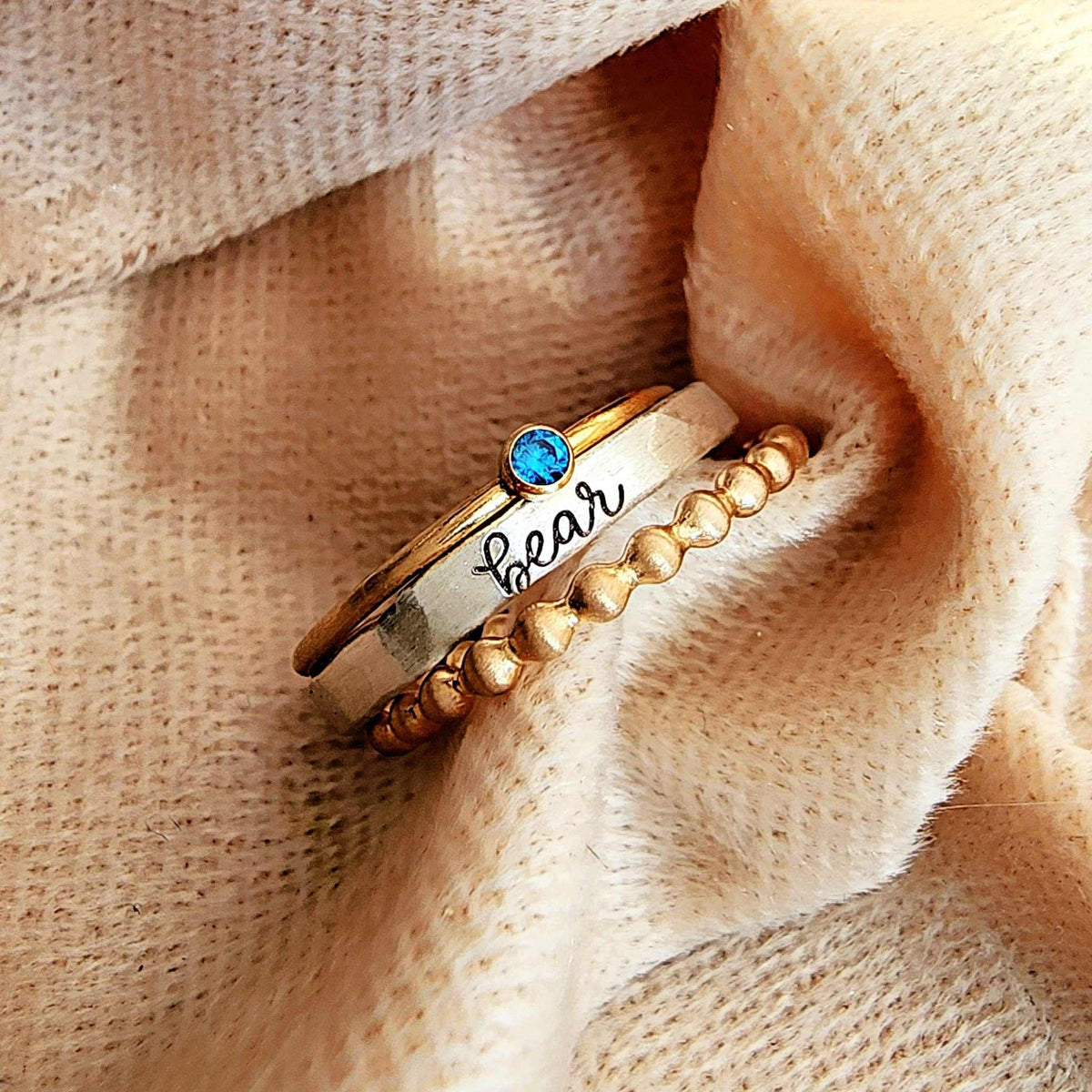 Gold ring with blue gemstone and 'bear' engraving on beige fabric