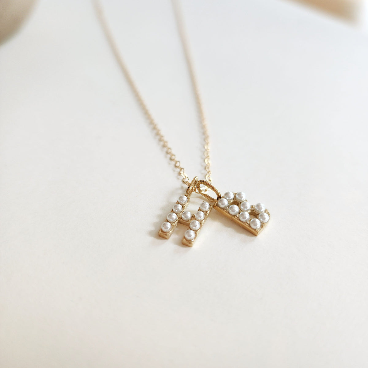 Gold necklace with a letter 'H' and "B" pendant on a light background